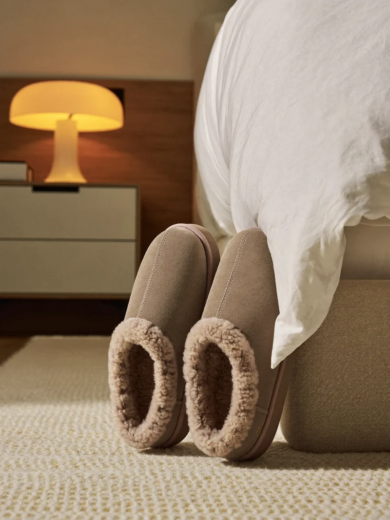 Chaussons doublés de peau lainée posés sur un tapis tressé près du lit